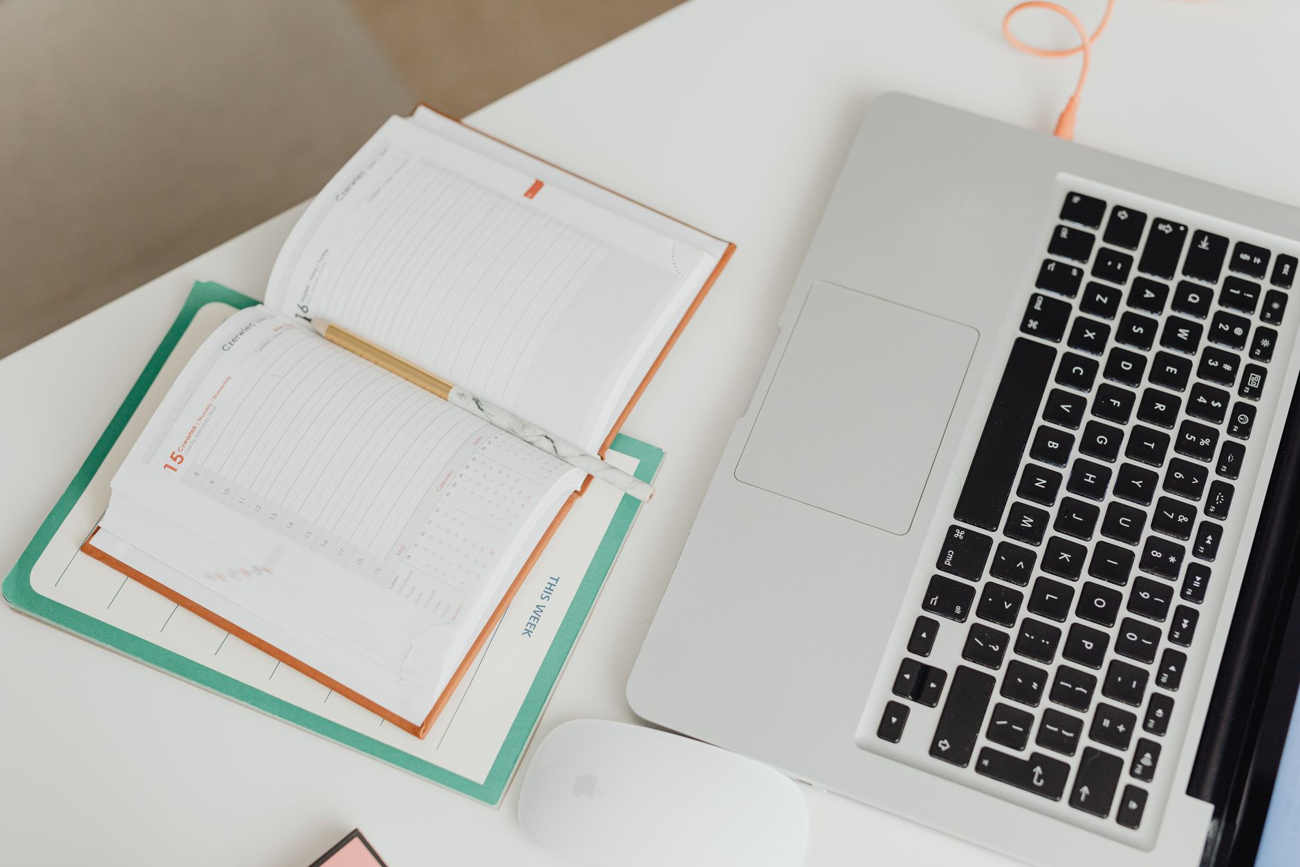 A person writing in a notebook beside a laptop showing a weekly calendar