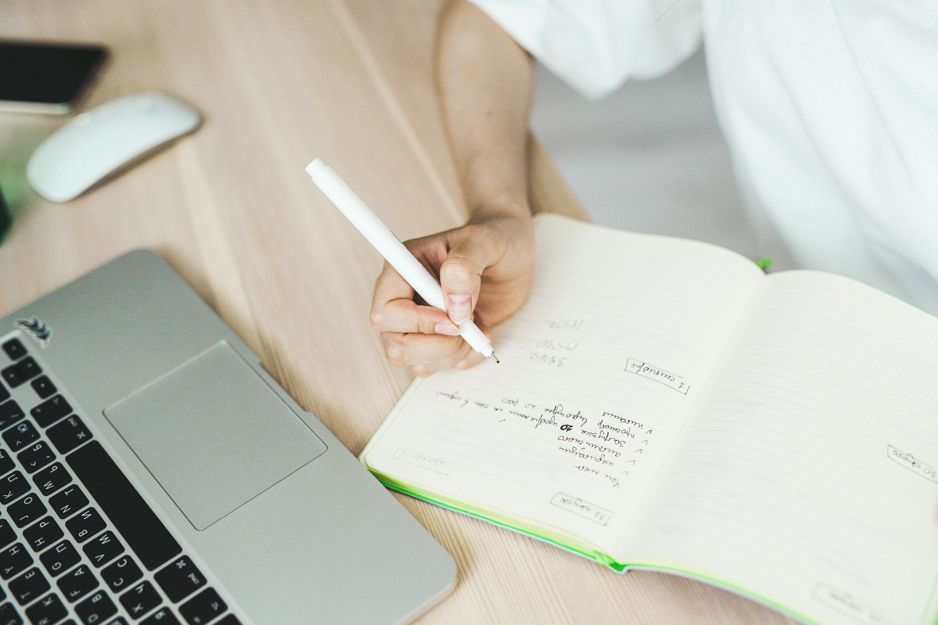 a person at a desk writing content ideas in a notebook with a coffee cup