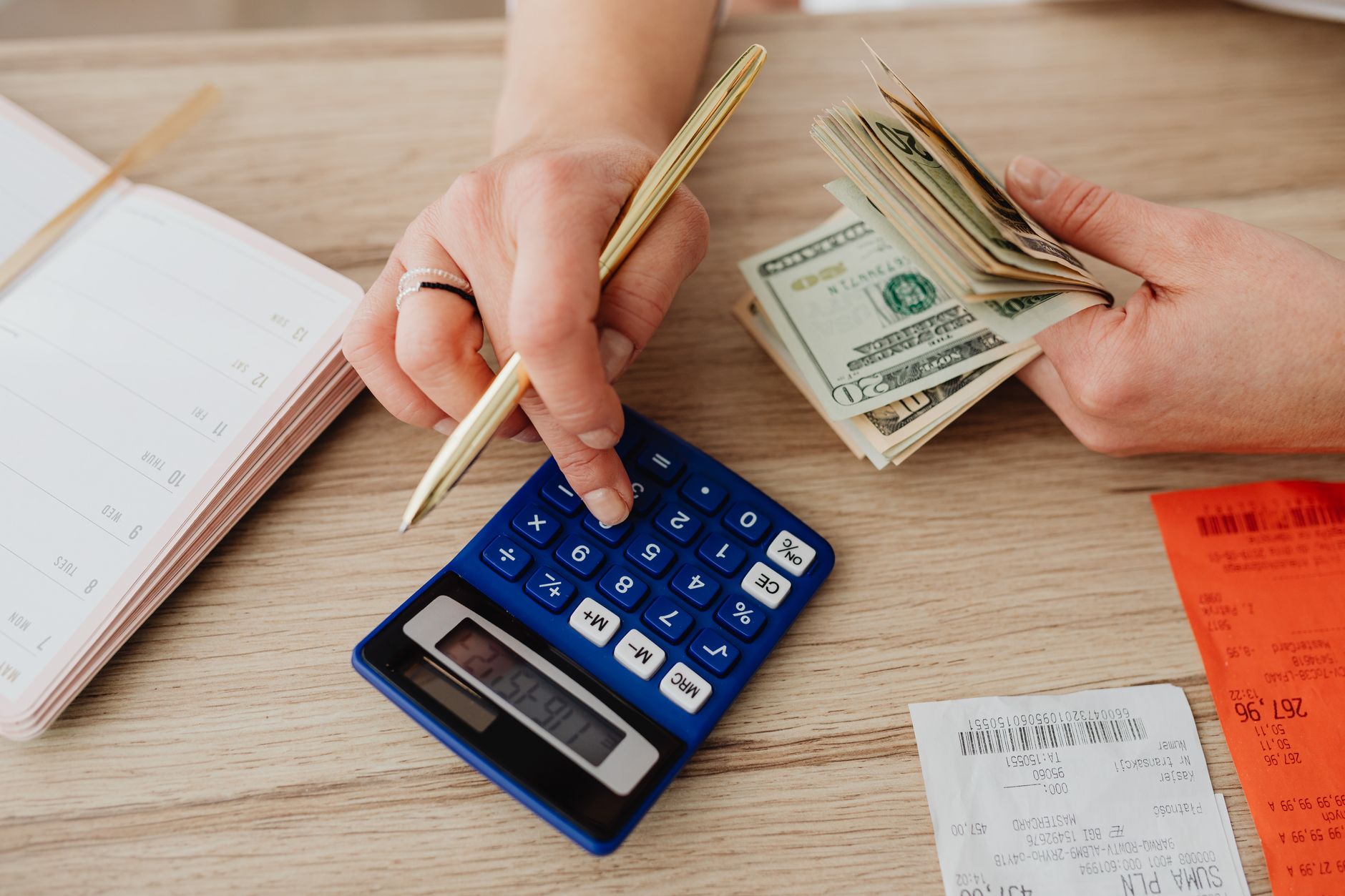 A person sitting at a desk calculating software subscription savings with a laptop and calculator.